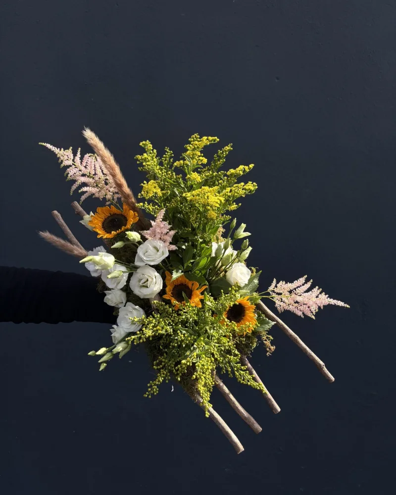 Bouquet d'automne d'atelier avec tournesols, solidage jaune, fleurs blanches et astilbe rose, tenu à la main sur fond sombre